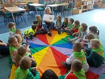Dzieci siedzą na chuście i słuchają opowiadania czytanego przez bibliotekarkę
