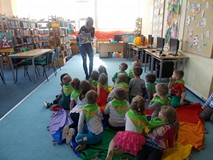 Dzieci siedząc na chuście odpowiadają na pytania obrazkowe, pokazywane przez bibliotekarkę