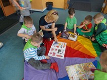 Nauczycielka siedzi z dziećmi na chuście i czyta im ksiązki