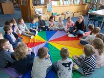 Dzieci siedzą na chuście i rozmawiają z bibliotekarką o książkach