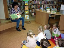 Bibliotekarka pokazuje dzieciom książeczkę z ilustrowanymi zagadkami