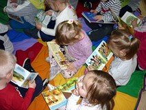 Dzieci siedzą na chuście integracyjunej i oglądają wybrane przez siebie książeczki
