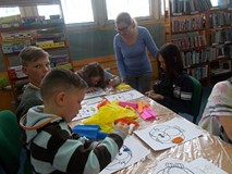 Dzieci siedzą przy stole i ozdabiają sowy biblułą