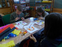 Troje dzieci siedzą przy stole i wykonują prace plastyczne