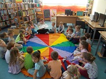 Dzieci siedzą na chuście i słuchają opowiadania czytanego przez bibliotekarkę