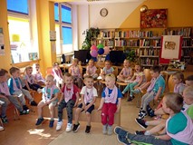 Dzieci siedzą na ławeczce i krzesełkach zasłuchane w opowieści o książkach