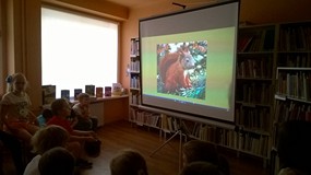 Dzieci siedzą na krzesłach i oglądają obrazy prezentacji