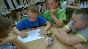 dzieci siedzą przy stoliku i piszą zakończenie poznanej bajki
