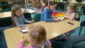 Dzieci siedzą przy stole i czytają z nauczycielką książeczkę