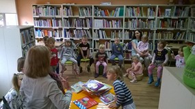 Dzieci siedzą w kole, a bibliotekarka prezentuje ciekawe książeczki