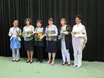 Sześć bibliotekarek stoi na scenie w rzędzie. Trzymają w ręku nagrody i odznaczenia oraz kwiaty