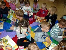 Dzieci siedzą na chuście integracyjnej i przeglądają wybrane przez siebie książeczki