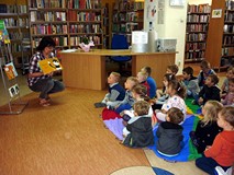 Dzieci siedzą na chuście integracyjnej, a bibliotekarka prezentuje ciekawe, interaktyne książeczki