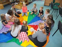 Dzieci i bibliotekarka  siedzą na chuście animacyjnej i grają w tic tac bum