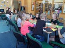 Dzieci siedzą przy stole i wykonują prace plastyczne