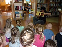 Dzieci siedzą na chuście integracyjnej, bibliotekarka pokazuje dzieciom 