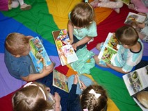 Dzieci siedzą na chuście integracyjnej i oglądają wybrane przez siebie książeczki
