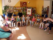 Bibliotekarka wita się z dziećmi, które siedzą na krzesełkach w kręgu