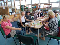 Panie siedzą przy stole i dyskutują o sztuce robienia na drutach