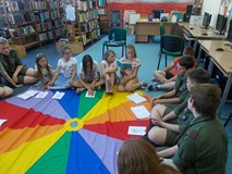 Harcerze siedża z dziećmi na chuście i wspólnie czytaja ksiązkę