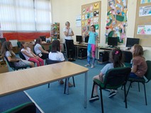 dzieci siedzą na krzesłach obserwując dziewczynkę, która pokazuje pantomimiczne hasło