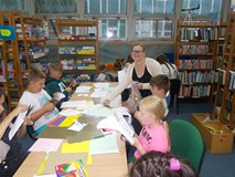 Bibliotekarka rozdaje materiały dzieciom wykonującymi prace dla ojców