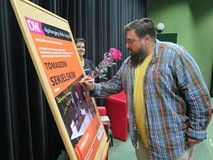 Tomasz Sekielski w Koszalińskiej Bibliotece Publicznej podpisuje plakat promocyjny.