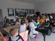 Dzieci siedzą przy stole i słuchają pana, który opowiada o kosmosie