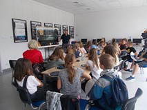 Dzieci wraz bibliotekarką siedzą przy stole i słuchają pana z Obserwatorium Astronomicznego, który o