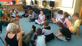 Dzieci siedzą w kręgu i prezentują swoją pracę plastyczną