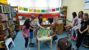 Bibliotekarka i dzieci występują w przedstawieniu teatru papierowego