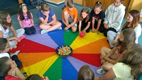 Dzieci z bibliotekarką siedzą na chuście i rzucają kostką