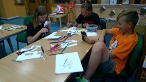 Troje dzieci siedzą przy stole i wykonują prace plastyczne