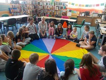 Dzieci siedzą na chuście z bibliotekarkami i prowadzącą warsztaty