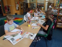 Dzieci siedzą przy stole i wyklejają wizytówki z gazet
