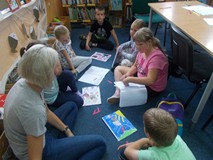 Dzieci siedzą na dywanie i dyskutują wspólnie z bibliotekarką