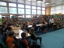 Dzieci siedzą przy stołach słuchając opowieści pisarza