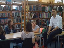 Dzieci siedzą przy stołach słuchając opowieści pisarza, który siedzi obok nich