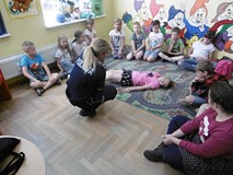 Filia nr 4. Dzieci siedzą w półokręgu w kuckach na dywanie podczas spotkania z policjantką na temat 