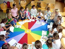 Filia nr 6. Dzieci siedzą w kole na kolorowej animowanej chuście, między nimi siedzi prowadząca wars