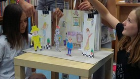 Filia nr 12. Dwie dziewczynki przy makiecie teatru. Wewnątrz makiety wykonane przez dzieci kukiełki 