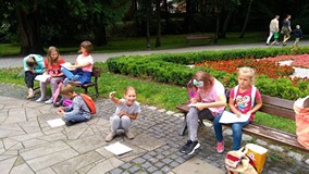 Filia nr 15. Dzieci siedzą na dwóch ławkach w parku i rysują to co widzą
