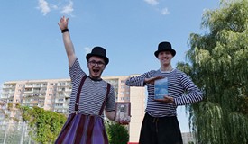 Dwaj panowie chodzący na szczudłach pomagają koszalińskim bibliotekarzom promować modę na czytanie. 
