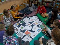 Dzieci siedzą na materacykach i utrwalają słownictwo związane ze szkołą.