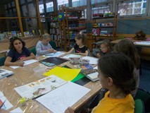 Dzieci siedzą przy stole podczas wykonywania pracy plastycznej