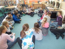 Uczniowie siedzą na dywanie w kole wspólnie z bibliotekarką