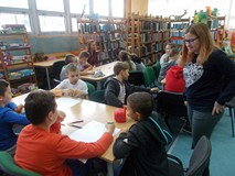 Dzieci pracują w grupach a bibliotekarka wspiera ich pracę