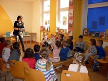 Dzieci siedzą na krzesełkach, bibliotekarka czyta pytania sprawdzające znajmość klasycznych baśni