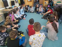 Dzieci siedzą na chuście animacyjnej i pokazują swoje imienne wizytówki