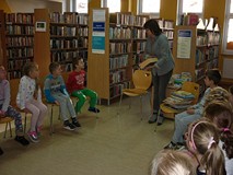 Dzieci siedzą na krzesełkach, bibliotekarka rozpoczyna prezentację książek z naszych zbiorów